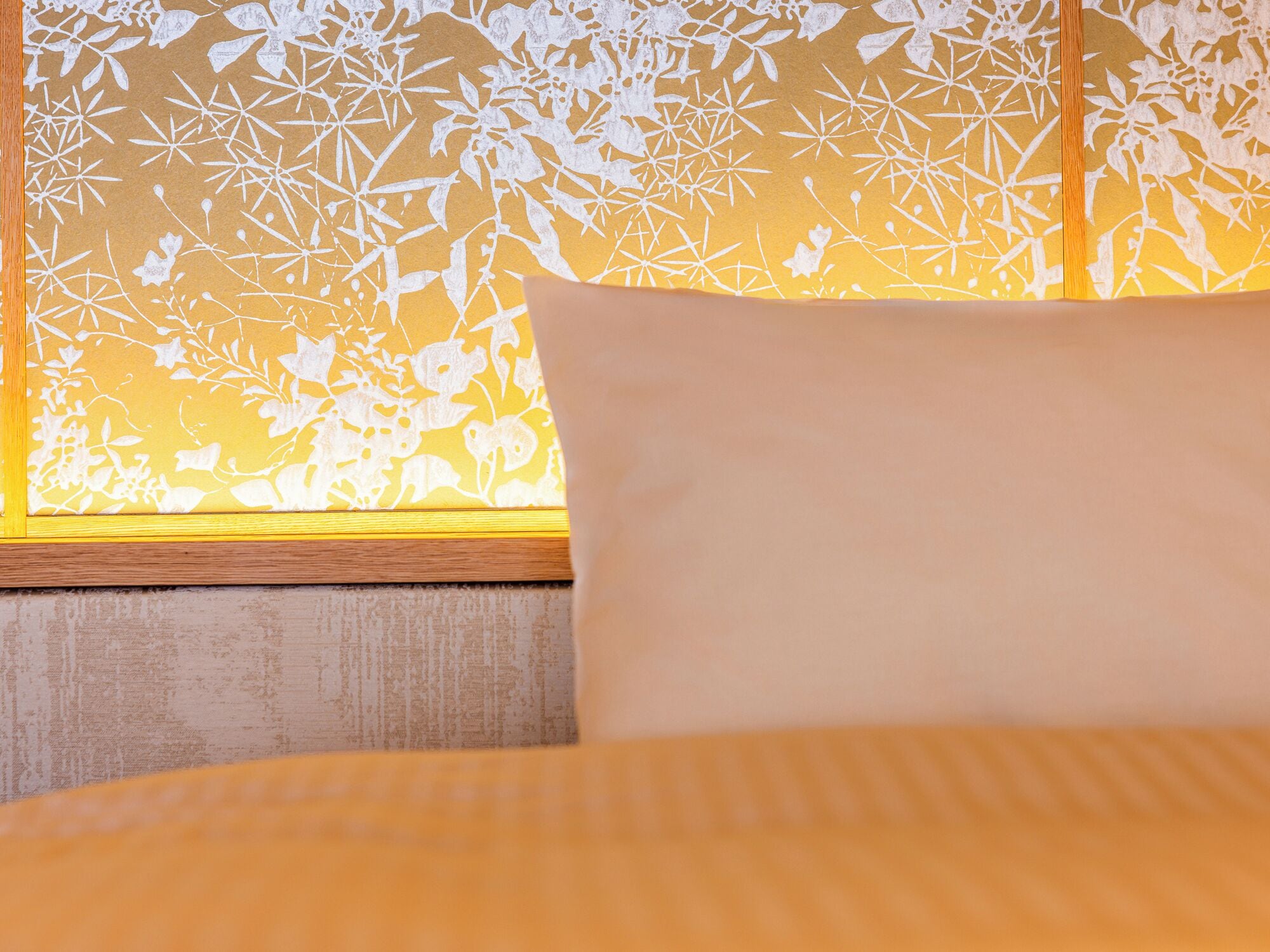 Un lit avec un oreiller blanc et une fenêtre ornée d’un store à motifs floraux.