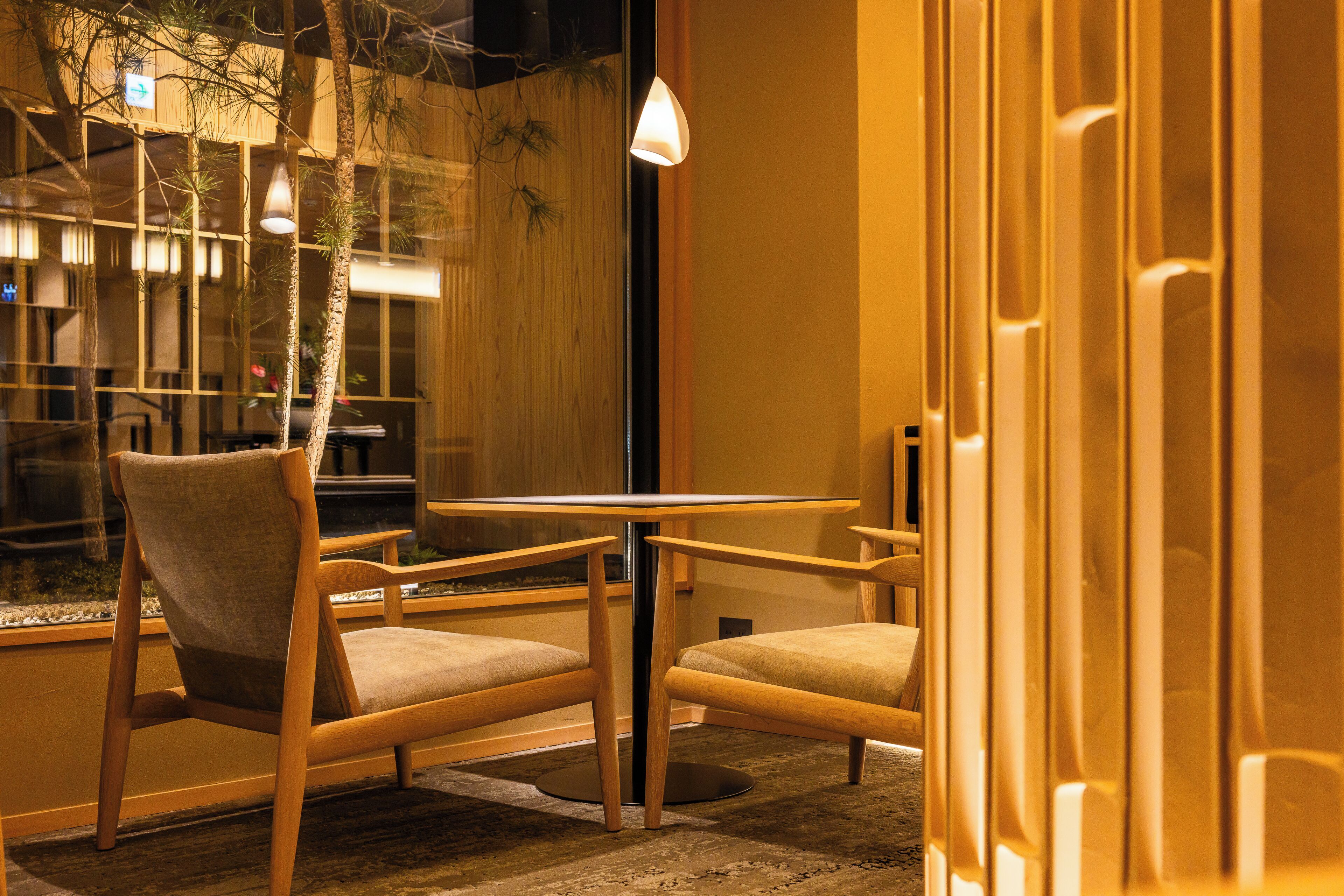 A cozy indoor seating area with wooden chairs and a small round table, featuring a view through a glass wall.