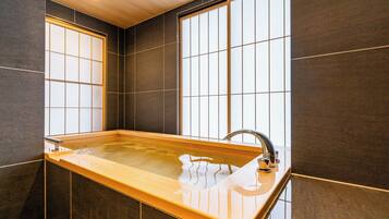 A modern bathroom with a large bathtub, dark tiled walls, and a window providing natural light.