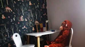 Una taula petita amb un joguet suau i un llibre, davant d'un paper pintat amb animals del bosc.
