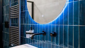 Un baño con azulejos azules, un espejo redondo, un perchero y un dispensador de jabón.