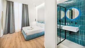 Un dormitorio moderno con cama, cortinas y un baño con lavamanos y espejo.