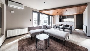 A modern living room with a sectional sofa, a round coffee table, and a kitchen area with a dining table and chairs. - JANUS villa Furano (Furano)