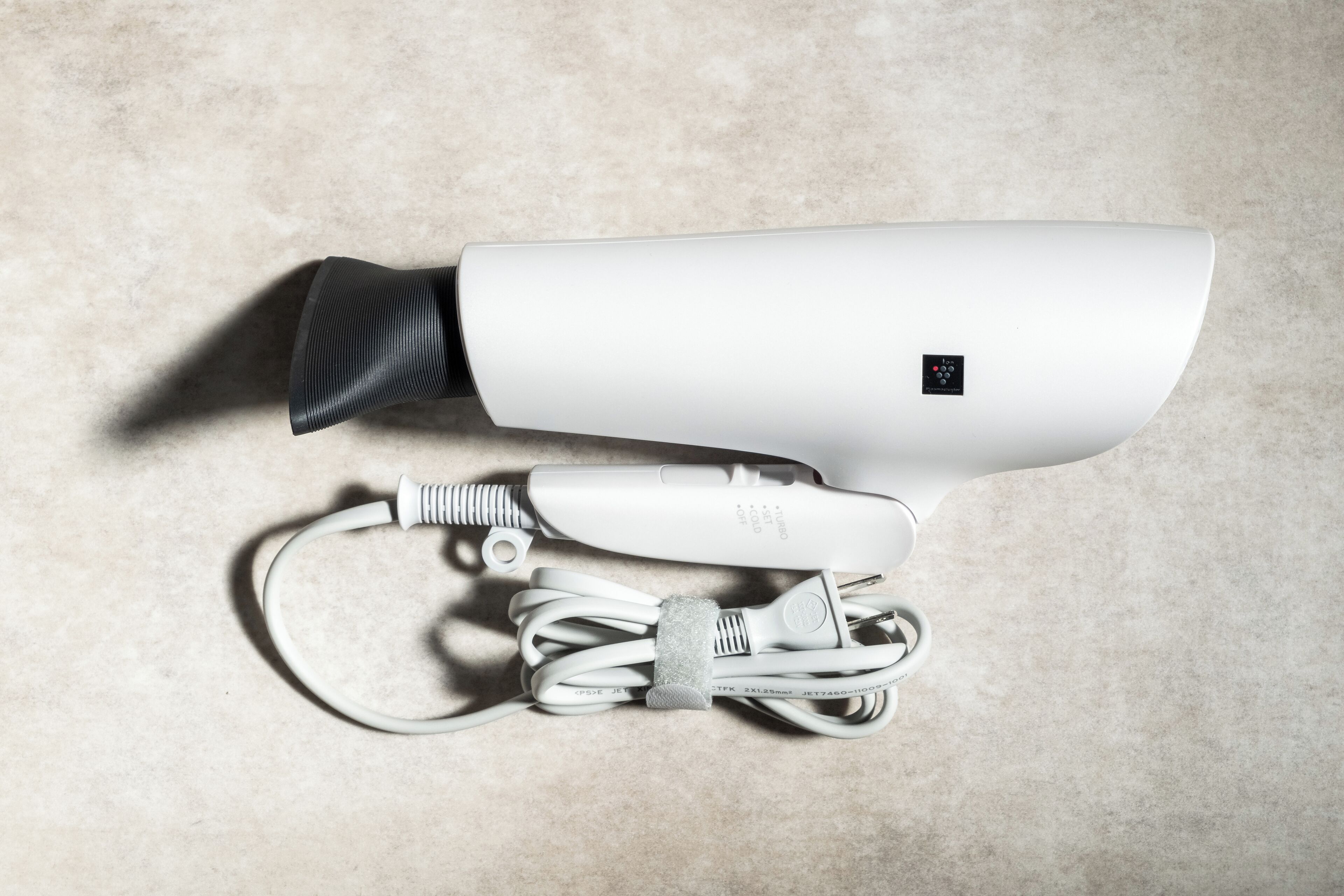 Een witte haardroger met snoer en een stroomadapter op een gestructureerd oppervlak.