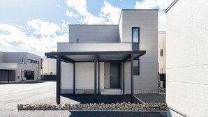 A modern building with a covered entrance, a clear sky, and a gravel pathway. - JANUS villa Furano (Furano)