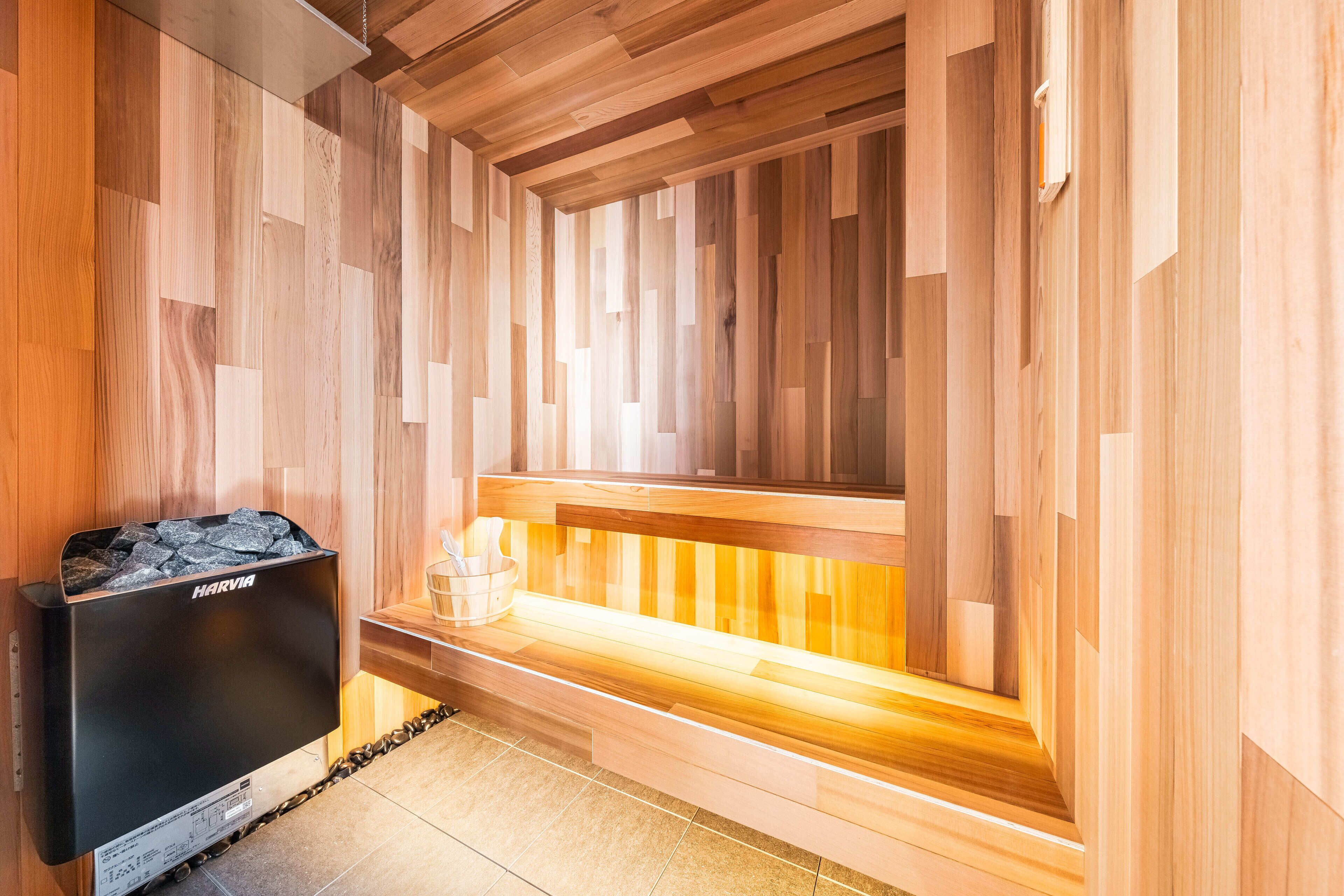 A sauna with a wooden bench and a Harvia sauna heater.