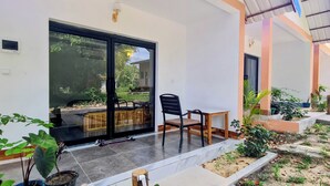 A modern house with a large sliding glass door, a small patio with a table and chairs, and a garden area with various plants. - Koh Rong Lagoon Bar And Restaurant  (Koh Rong)