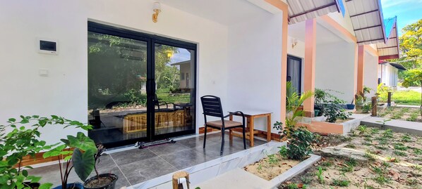 A modern house with a large sliding glass door, a small patio with a table and chairs, and a garden area with various plants. - Koh Rong Lagoon Bar And Restaurant (Koh Rong)