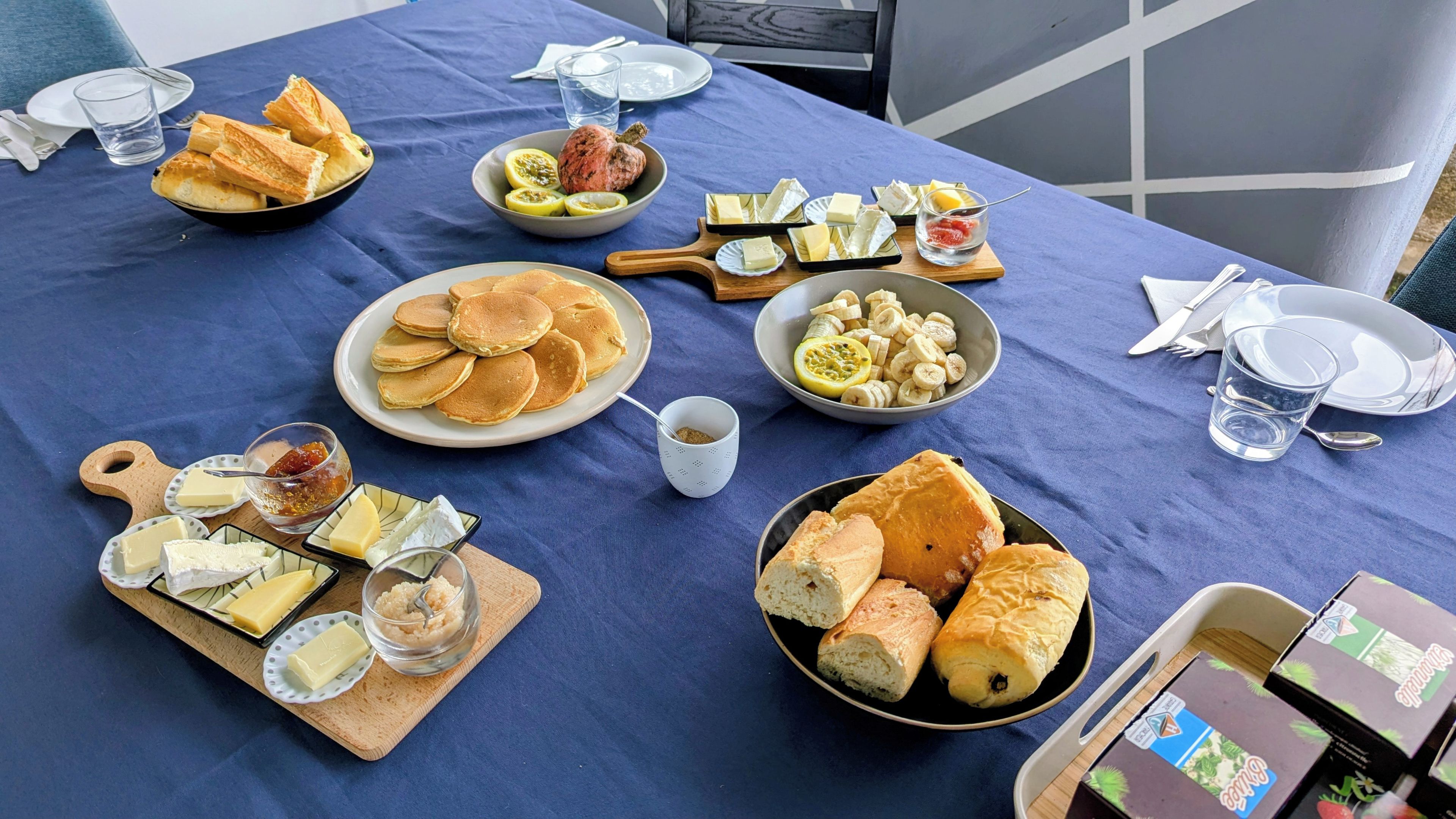 Una mesa servida con diferentes alimentos, incluyendo pan, queso y frutas, que sugiere un desayuno o una merienda.
