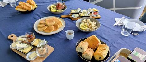 Ein Tisch reichhaltig mit Speisen gedeckt, darunter Brot, Käse und Obst – ein Angebot für Frühstück oder einen kleinen Imbiss.