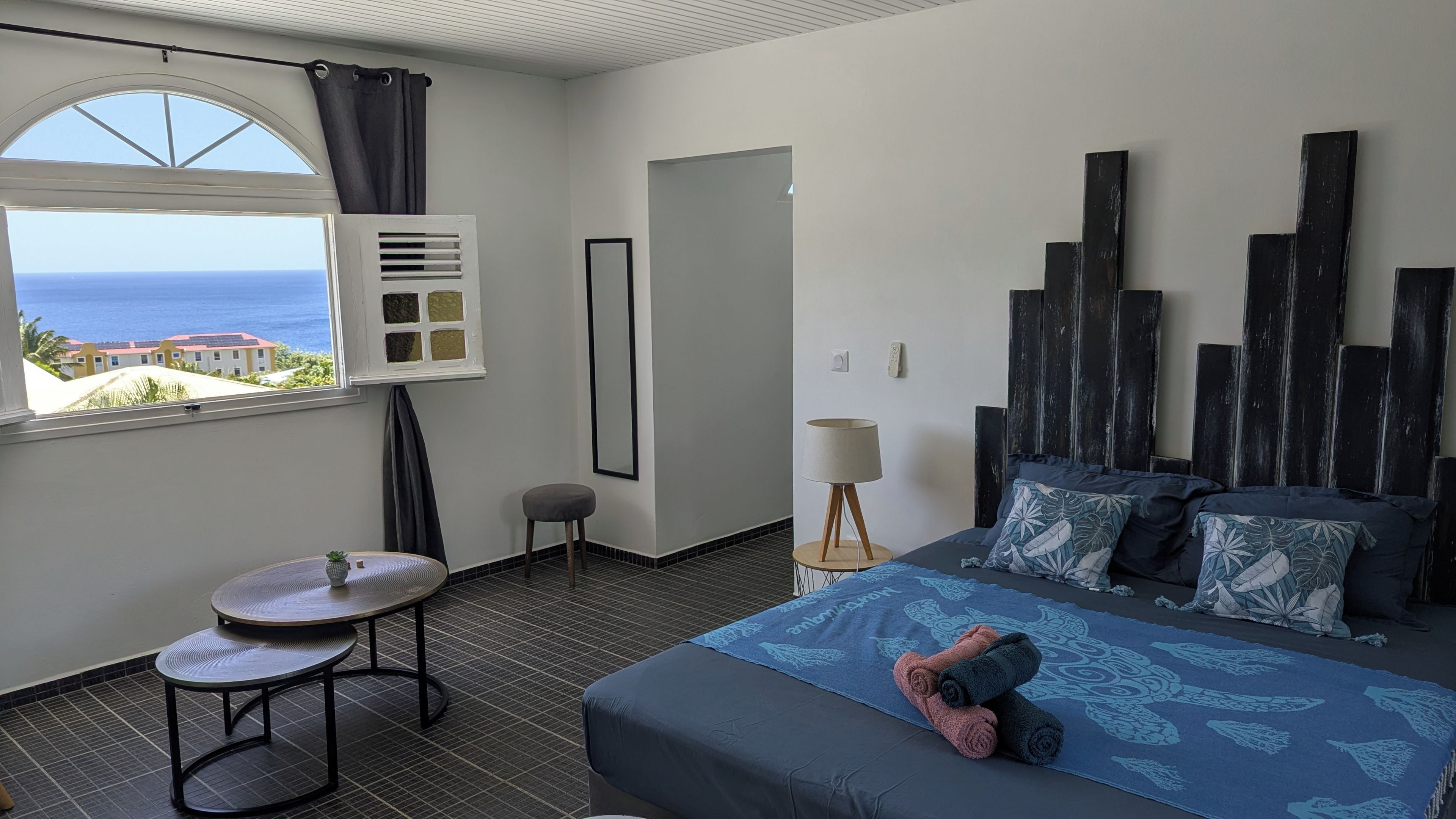 Une chambre d’hôtel avec un lit, une petite table, une chaise, une fenêtre donnant sur la mer et un climatiseur fixé au mur.