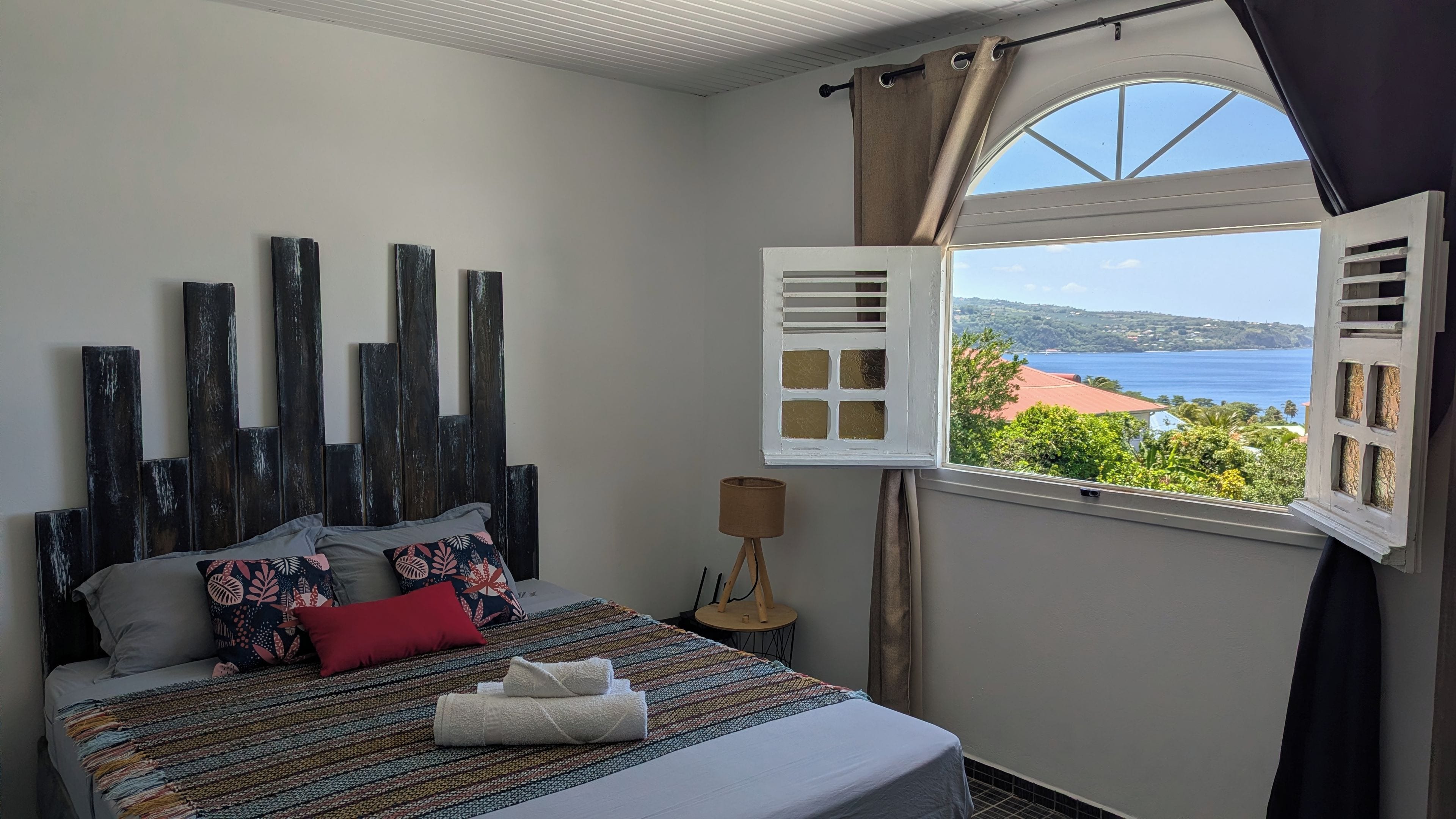A bedroom with a bed, a view of the sea, and a window with curtains.