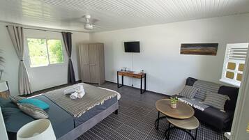 Habitación de hotel con cama, sofá, una mesita, televisor y ventana con cortinas.