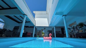 A swimming pool with a pink flamingo float, surrounded by white columns and a covered area with chairs and tables. - L'Hacienda (Saint-Pierre)