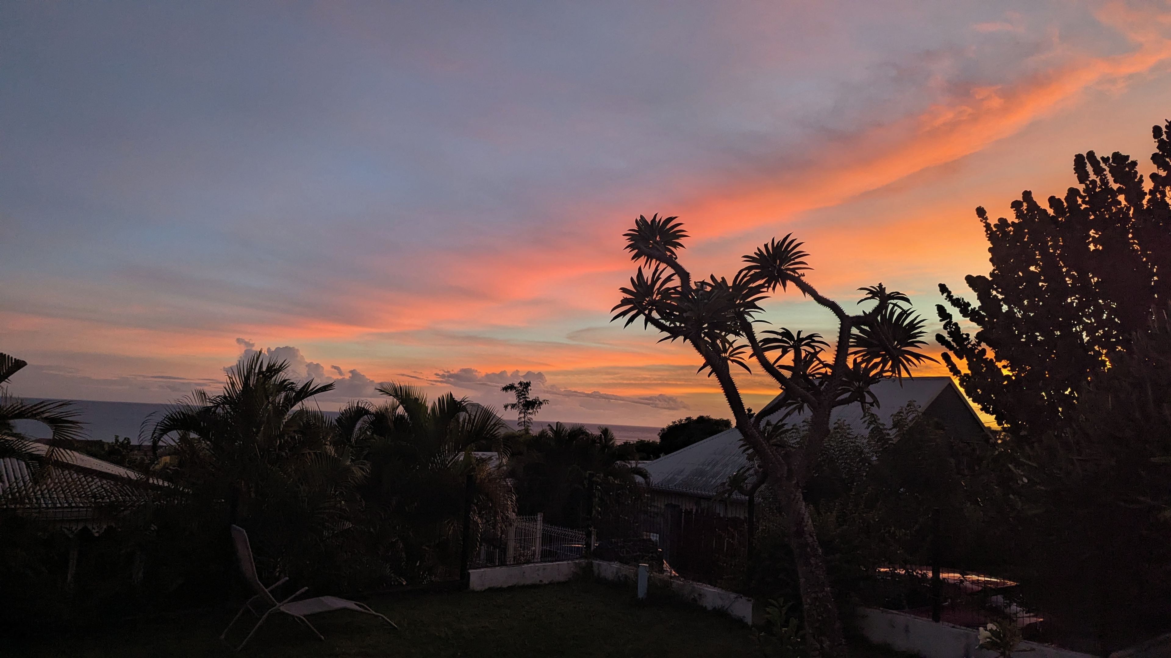 A sunset with silhouettes of palm trees and a house.