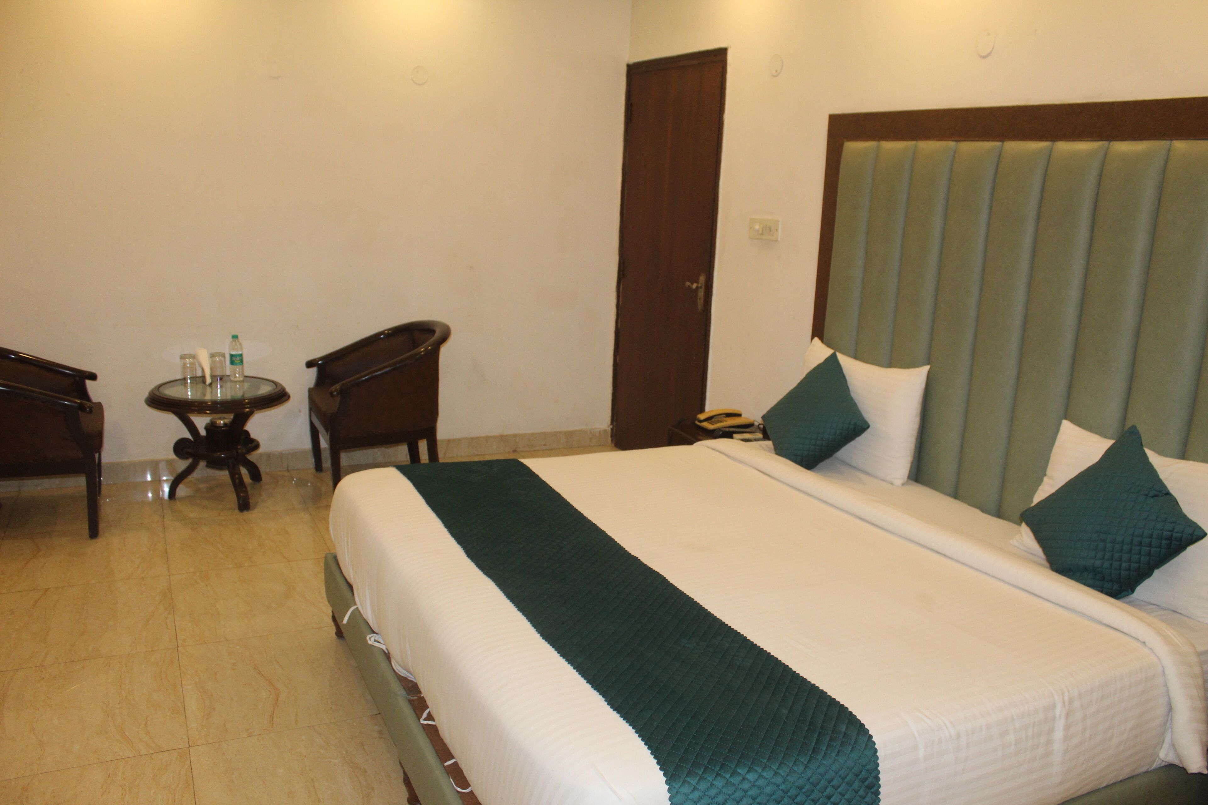 A hotel room with a bed, a small table with a chair, and a door.