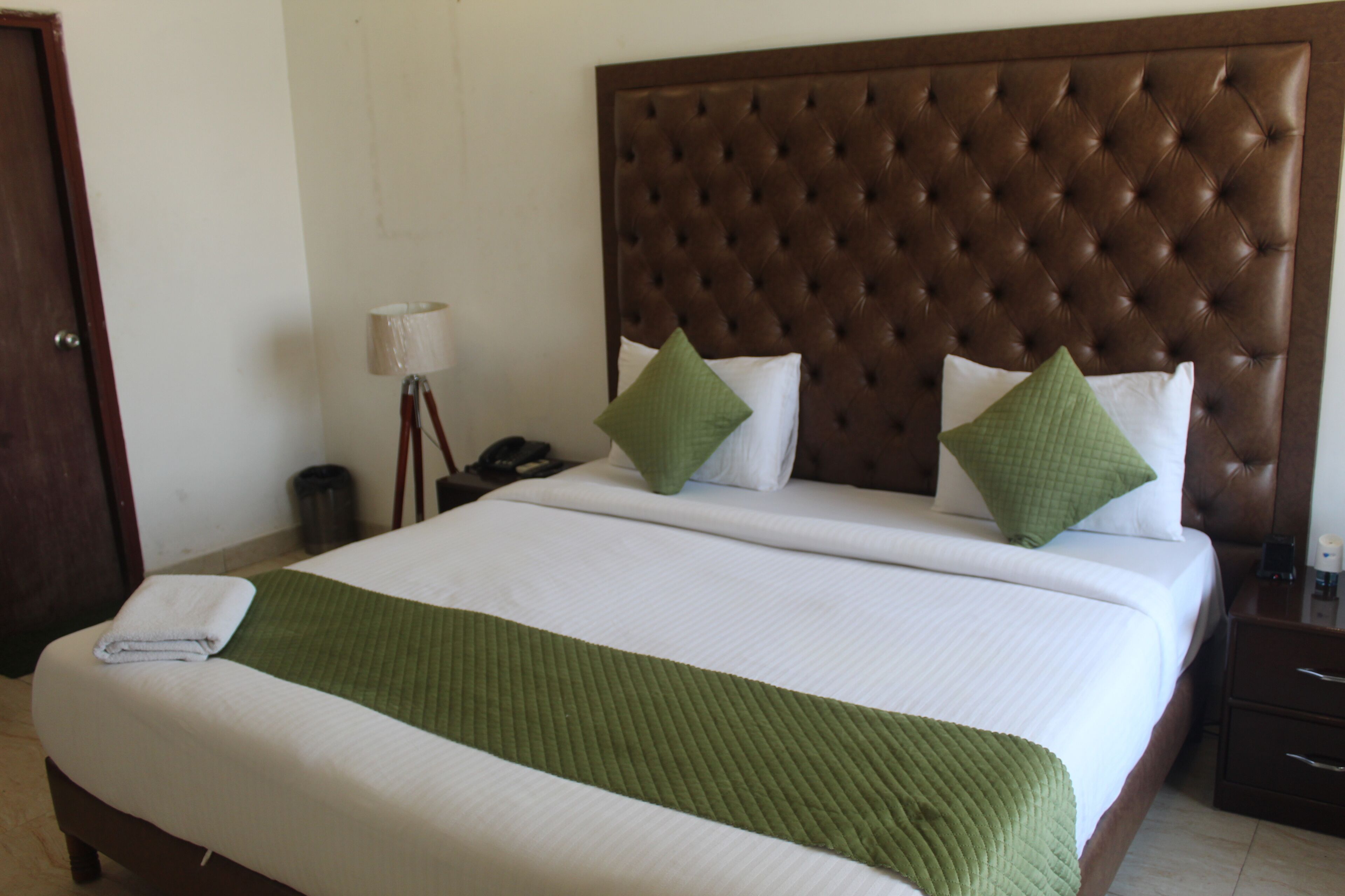 A neatly made bed with a green bedspread, a brown headboard, and two green pillows.