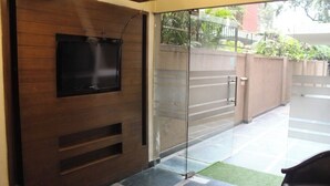 Un intérieur moderne avec un téléviseur à écran plat fixé sur un mur en panneaux de bois, une porte vitrée donnant sur l’extérieur et un sol carrelé.