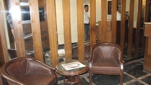 Un hall d’entrée avec deux fauteuils en cuir, une table ronde sur laquelle repose un journal et une cloison en bois composée de lattes verticales.