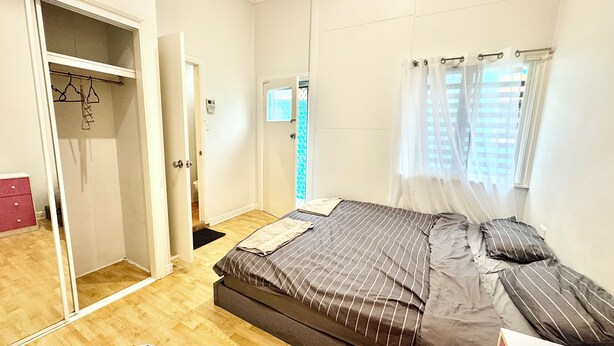 A bedroom with a bed, a wardrobe, and a window with curtains. - Studio Room Ensuite Bathroom with Separate Entrance (Woolloongabba)