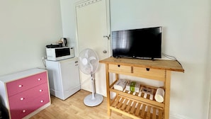 A room with a wooden TV stand, a microwave, a refrigerator, a pink dresser, and a standing fan. - Studio Room Ensuite Bathroom with Separate Entrance (Woolloongabba)