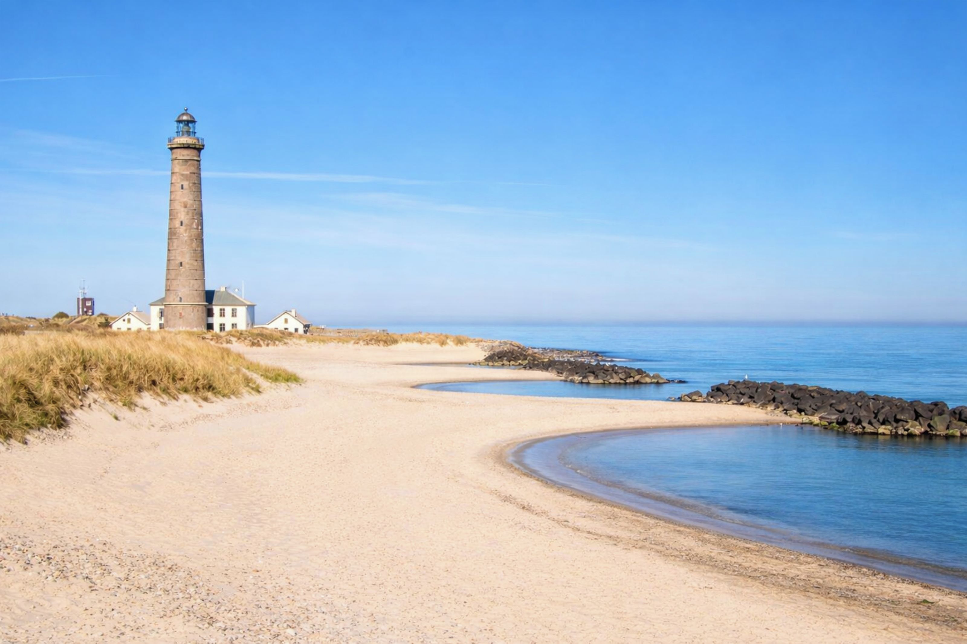 A coastal path leading to a lighthouse, with a clear sky and calm sea.