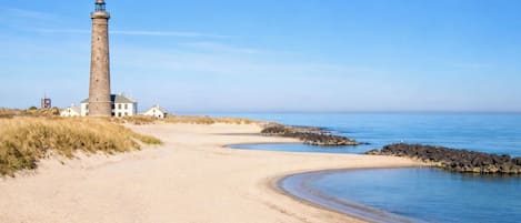 A coastal path leading to a lighthouse, with a clear sky and calm sea.