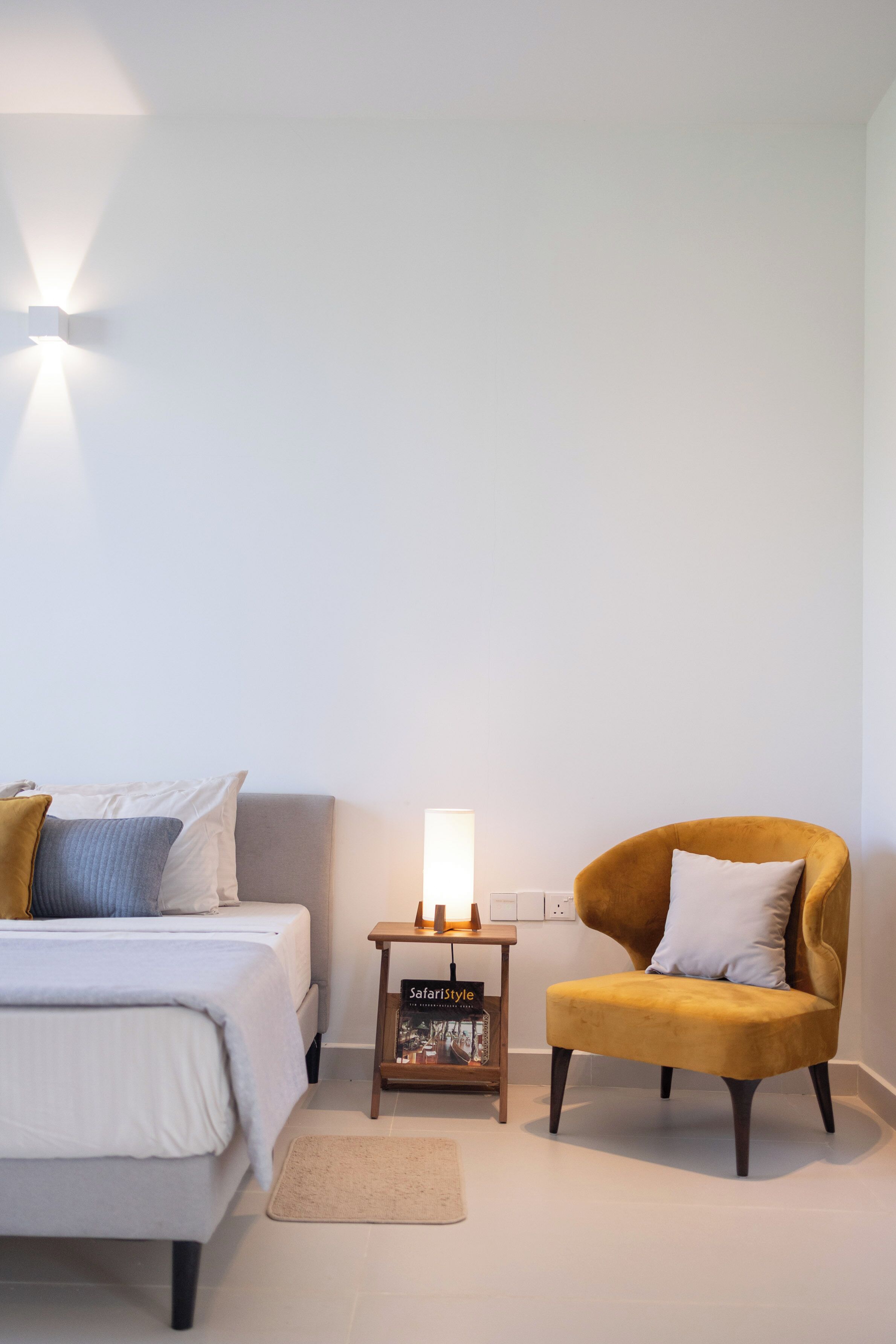 A bedroom with a bed, a nightstand with a lamp, a chair, and a small table with a book.