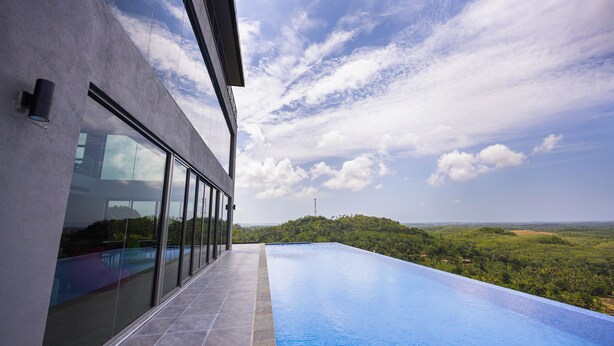 A modern building with a large glass window and a rooftop infinity pool overlooking a lush landscape. - Starlit A Luxury Hilltop Villa with Infinity Pool & Chef (Udukawa)