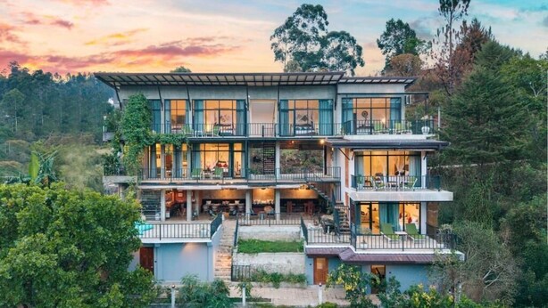 Une maison à plusieurs étages, dotée d’un balcon à chaque niveau, et entourée d’une végétation luxuriante.