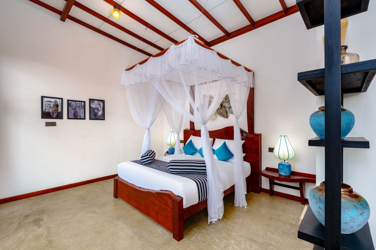 A four-poster bed with white bedding and blue pillows, a wooden headboard, and a canopy. There are two bedside tables with lamps and decorative vases.