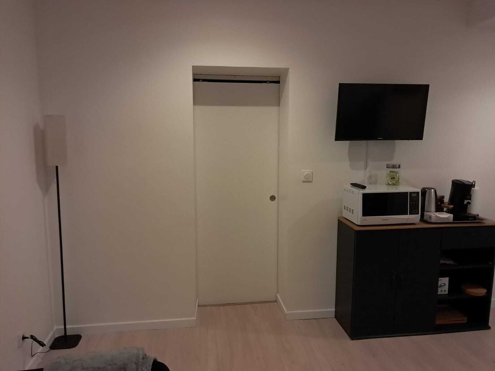 Ein Zimmer mit einer weißen Tür, einem an der Wand befestigten Flachbildfernseher, einer Mikrowelle und einer Kaffeemaschine auf einem Holzschrank.
