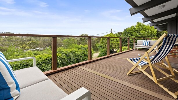 Une terrasse en bois, agrémentée de mobilier d’extérieur, notamment d’un canapé et de fauteuils de jardin à rayures, qui offre une vue sur un paysage luxuriant.