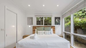 Une chambre moderne avec un cadre de lit en bois, une literie blanche et une vue sur la verdure grâce à de grandes fenêtres.