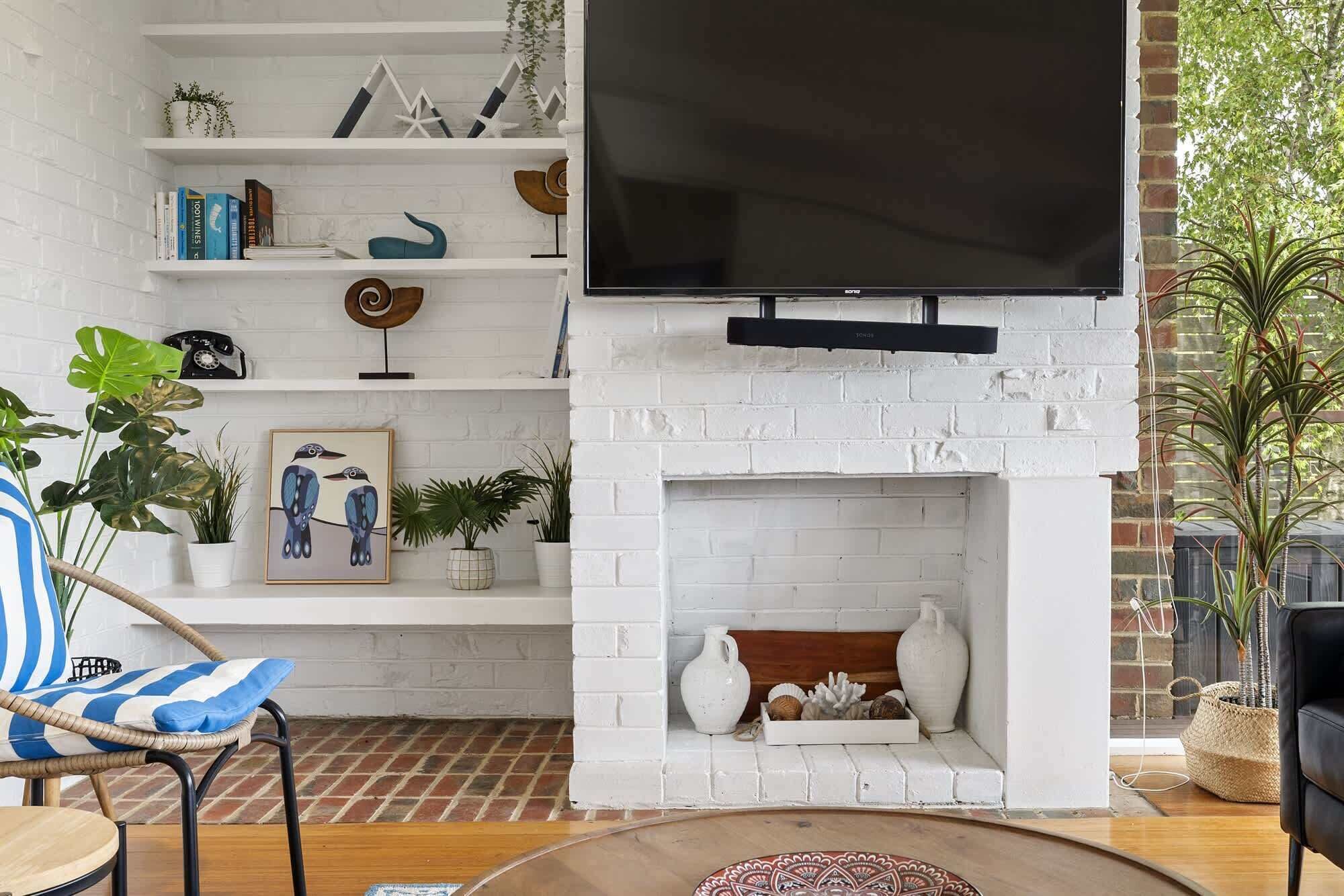 A living room with a white brick fireplace, a mounted TV, and a bookshelf with decorative items.