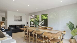 Un vaste espace de vie comprenant une table à manger, des chaises, un canapé et une grande fenêtre donnant sur un paysage verdoyant.