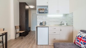 A compact kitchen with a refrigerator, microwave, and kettle. There is a dining table with chairs and a small sofa with a pillow. - MaRKoS Flat 202 in Loft 2, floor 2, New Gudauri (Gudauri,)