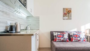 A compact kitchen with a kettle, a coffee maker, and a sink. A bed with a pillow featuring the London flag is visible. - MaRKoS Flat 202 in Loft 2, floor 2, New Gudauri (Gudauri,)