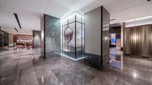 A modern lobby with a glass elevator, marble flooring, and contemporary furnishings. - Yicheng Hotel Wuzhou City Government  (Wuzhou)