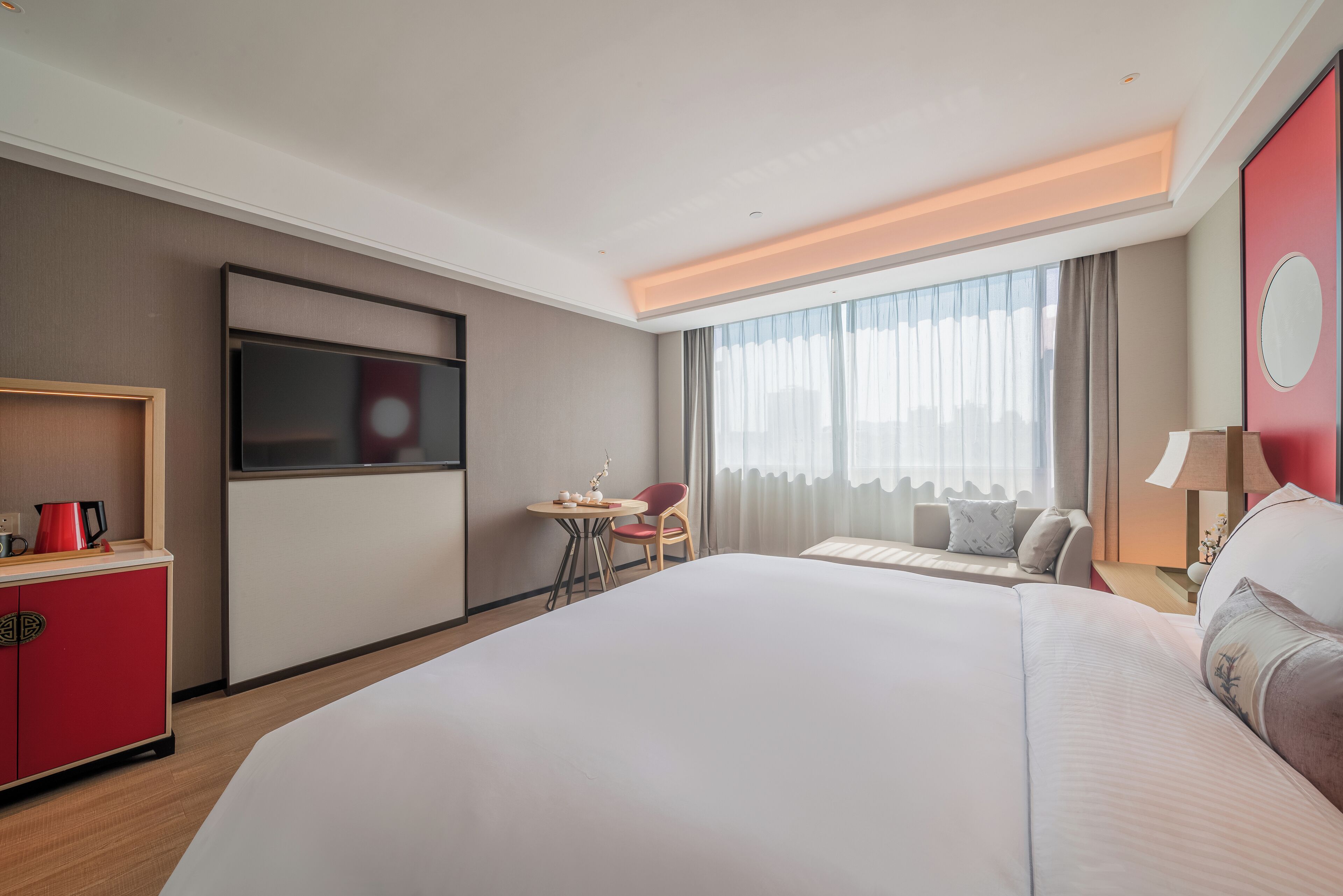 Habitación de hotel con una cama grande, televisión, escritorio con silla, un armario rojo y una ventana con cortinas.