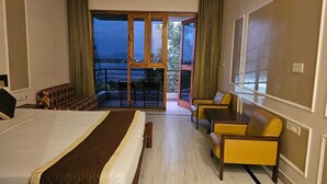 A hotel room with a large bed, a sofa, a table, and chairs. There is a balcony with a view of the outdoors. - Kanota Camp Resort (Jaipur)