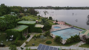 A landscaped area with a swimming pool, solar panels, and a view of a lake. - Kanota Camp Resort (Jaipur)