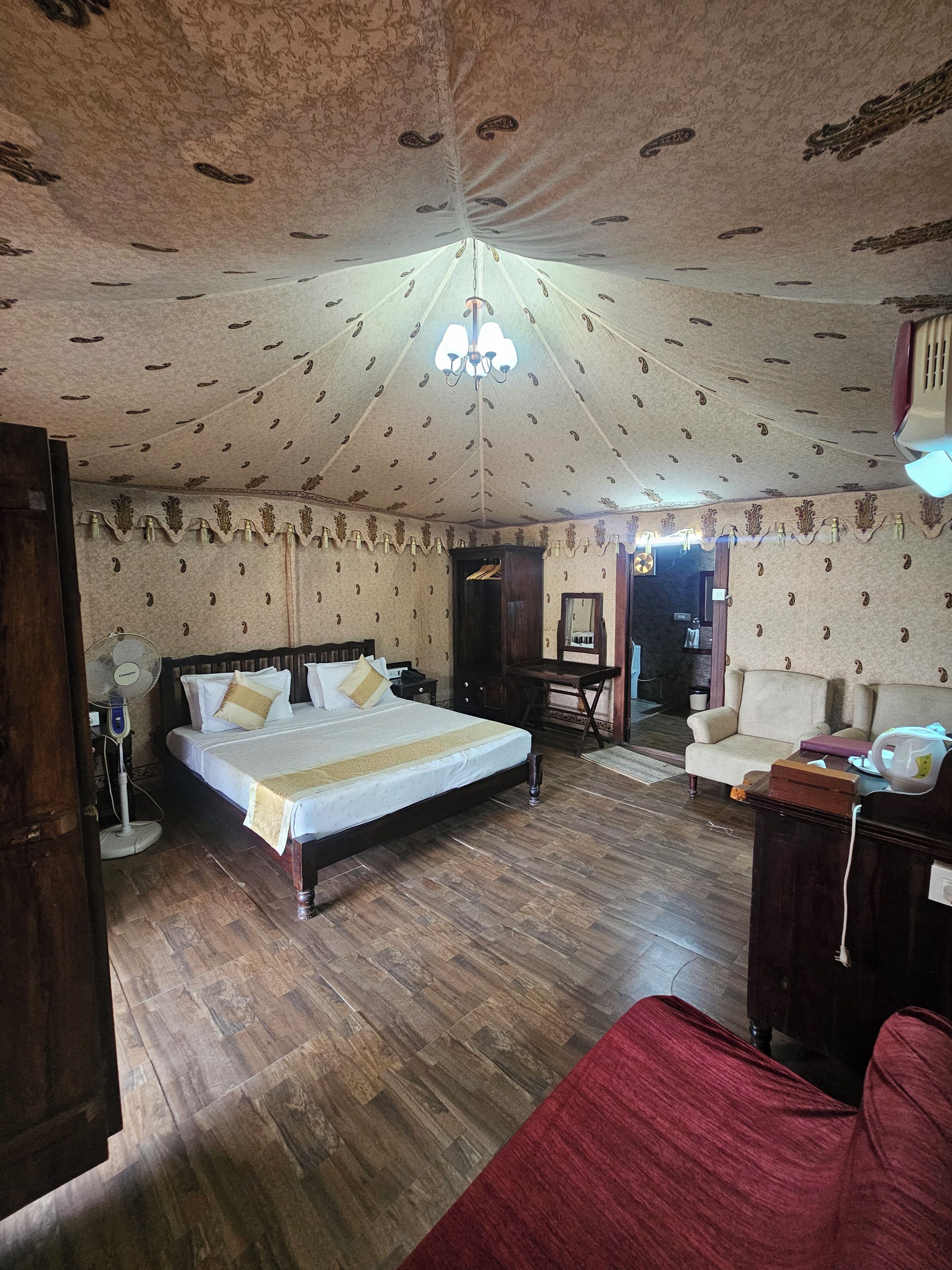 A room with a large bed, a wooden floor, a ceiling fan, and a chandelier.
