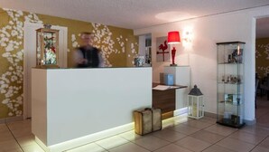 A reception area with a counter, a glass cabinet, a red lamp, and a vintage suitcase. - LOGIS HOTEL LE PARC DE GEOFFROY (Thiers)