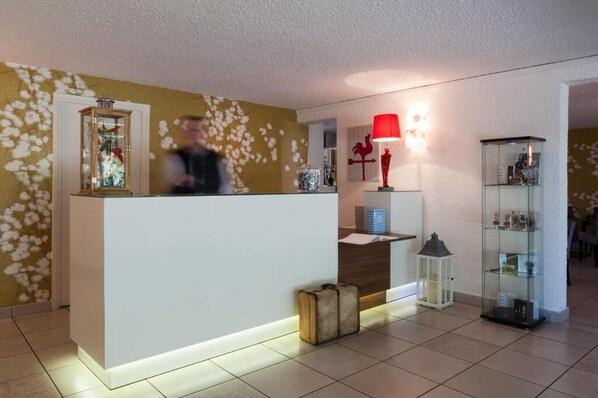 A reception area with a counter, a glass cabinet, a red lamp, and a vintage suitcase. - LOGIS HOTEL LE PARC DE GEOFFROY (Thiers)