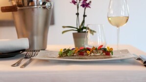 A dining table with a plate of food, a glass of white wine, a metal bucket, and a potted plant. - LOGIS HOTEL LE PARC DE GEOFFROY (Thiers)