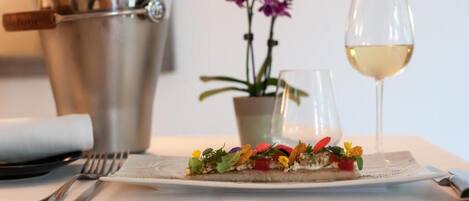 A dining table with a plate of food, a glass of white wine, a metal bucket, and a potted plant.