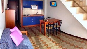 Un espacio habitable compacto con kitchenette, comedor y una escalera.