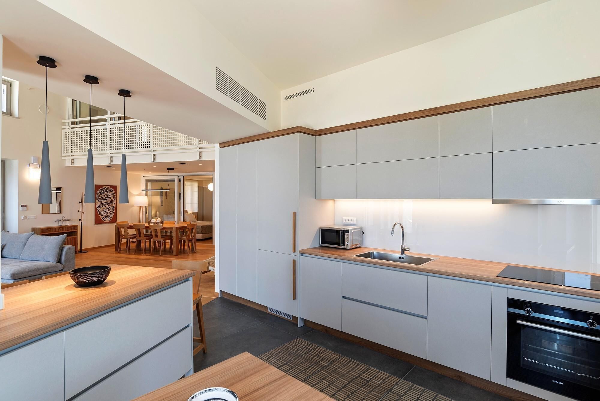 Una cucina moderna con mobili bianchi, forno a microonde integrato e forno Siemens. C'è un'area pranzo con tavolo e sedie in legno, e una scala che conduce a un piano superiore.