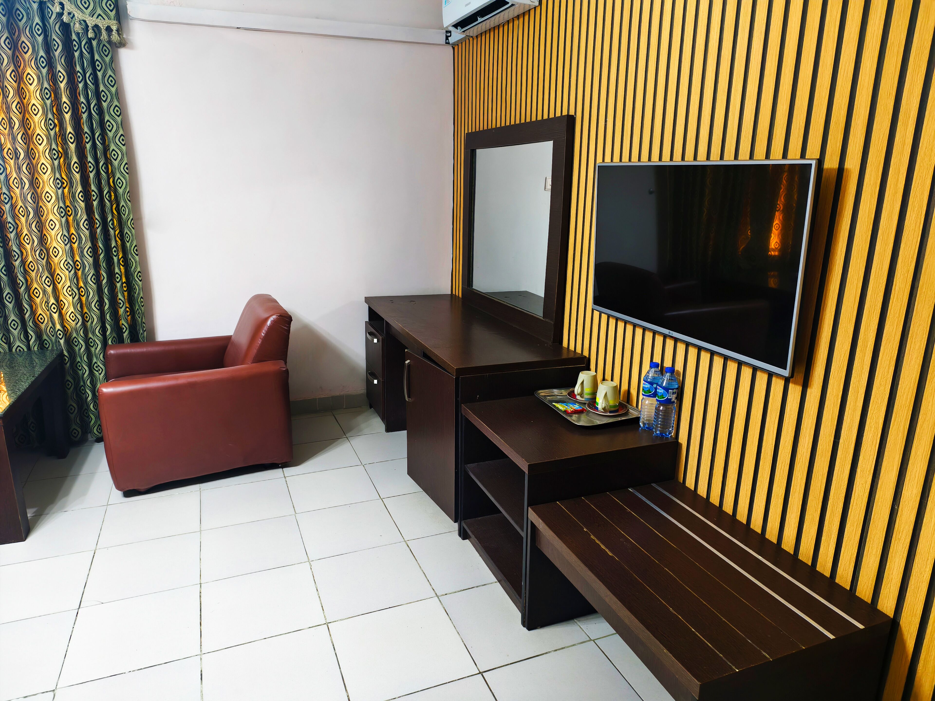 A hotel room with a sofa, a desk, a TV, and a tray with cups and bottles.